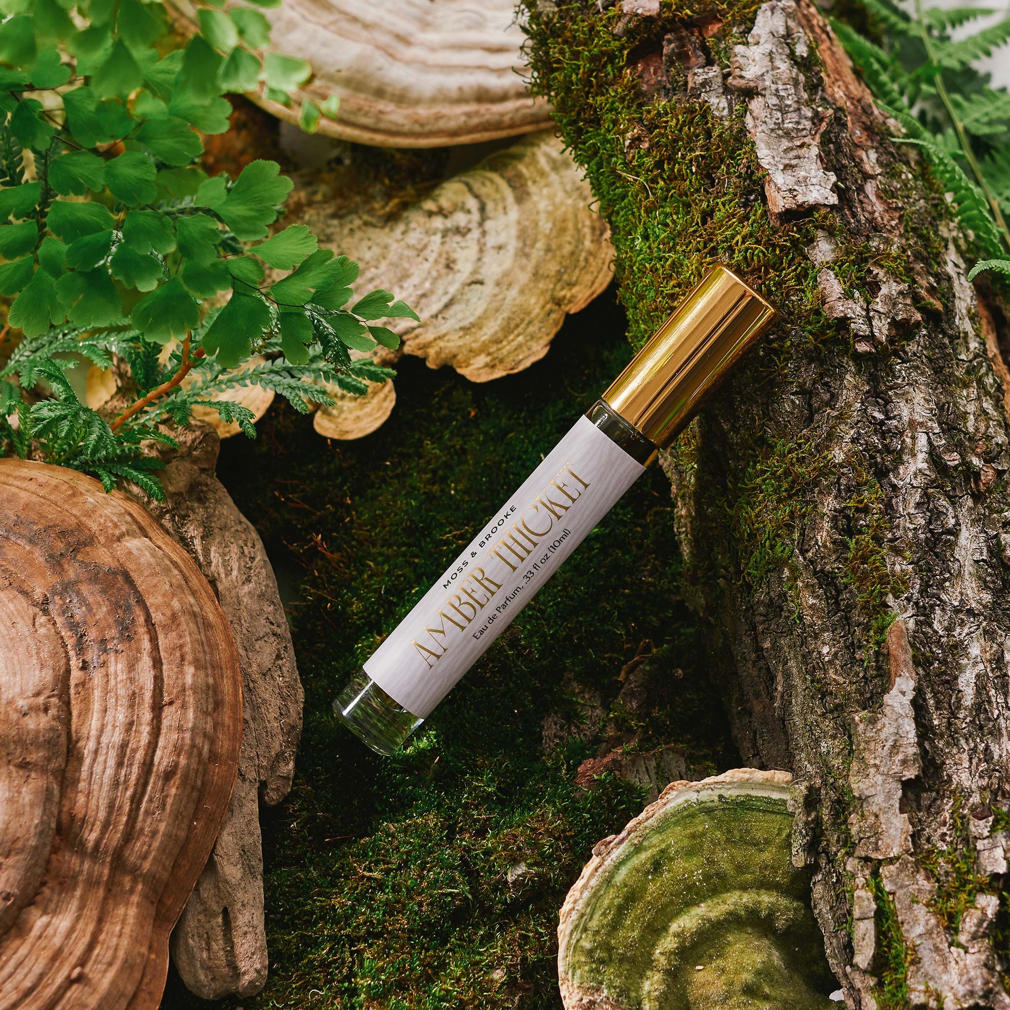 Slim round glass bottle with gold cap and gray label with metallic gold text. Amber Thicket natural botanical perfume is scented with linden, beeswax, apricot, bergamot, hay, patchouli and ylang ylang. 